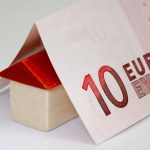 kredit fuer haus - 10 Euro schein liegt gefaltet über einem kleinen Holz-Häuschen Modell